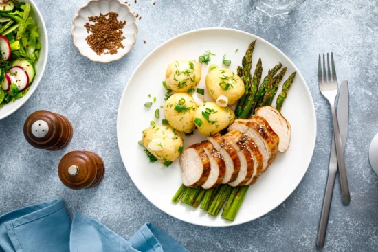 Professionally plated sliced pork loin with herb-roasted potatoes and grilled asparagus, ideal for fine dining food service and culinary supply applications.