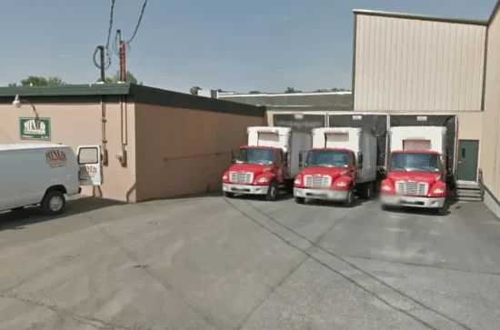Red box trucks at warehouse loading bays under clear daylight sky.